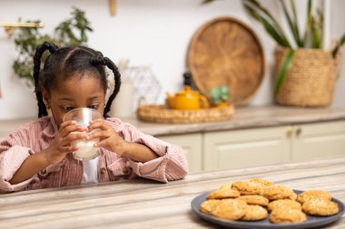 Mutlu Afrikalı Amerikalı çocuk evde kurabiyelerle süt içiyor.