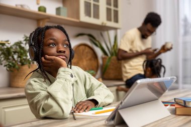 Afro-Amerikalı küçük kız ödevlerini evde çalışırken tablet kullanarak yapıyor.