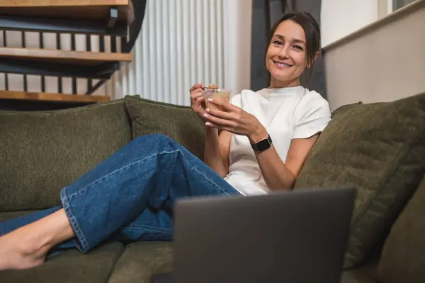 Stock image Happy woman. Contented young woman sitting on the sofa and eating dessert