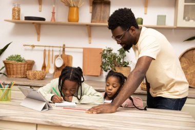 Afro-Amerikalı baba ve kız evde tablet kullanarak ödev yapıyorlar.