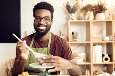 Hobi olarak. Gülümseyen adam çanak çömlek boyuyor ve bakıyor.