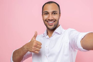 Beyaz gömlekli gülümseyen adam pembe arka planda izole edilmiş bir jest görüntüsü veriyor.