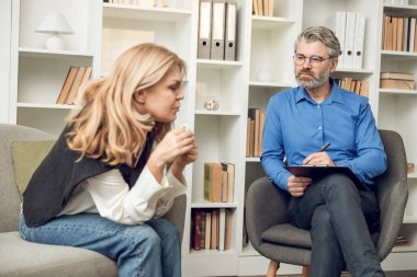Kendine güvenen bir psikolog, sorunlu kadın hastasıyla ofisinde çözümleri ve desteği tartışıyor.
