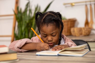 Evde üzgün bir ifadeyle egzersiz defterine yazı yazan çok kültürlü bir kız.