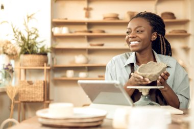 Çevrim içi atölye. Memnun Afrikalı Amerikalı kadın çevrimiçi atölyede seyirciye kilden kavanoz gösteriyor.
