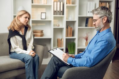 Kendine güvenen bir psikolog, sorunlu kadın hastasıyla ofisinde çözümleri ve desteği tartışıyor.