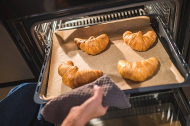 Taze kruvasan. Kadınların ellerinin tepsiyi fırından kruvasanlarla çıkardığı resmi kapat.