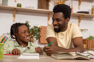 Neşeli siyah baba ve kızı okul işlerini birlikte yapıyorlar.