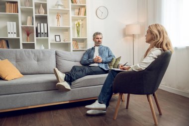 Mutsuz bir adam danışmanlık ofisinde kanepede oturup kadın psikoloğa dertlerinden yakınırken o da not alıyor.