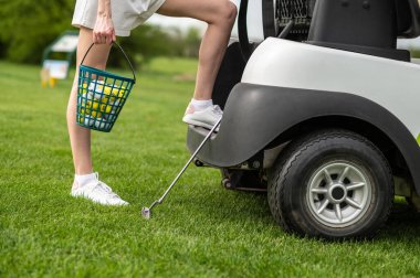 Tanımlanamayan beyaz kadın golfçü golf arabasının yanında yeşil üzerinde poz veriyor.