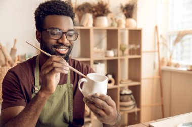 Çömlek. Koyu tenli bir adam yeni bir çömlek fırçalıyor ve memnun görünüyor.