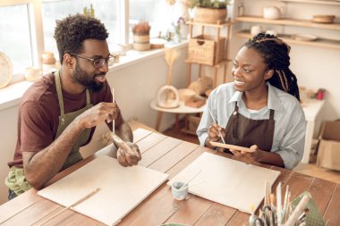 Çömlek atölyesi. Afrika kökenli Amerikalı erkek heykeltıraş çömlekçilik atölyesindeki bir kız öğrenciye bir şey anlatıyor.