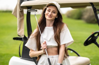 Aktif beyaz kadın, doğasında golf olan aracın yanında duruyor.