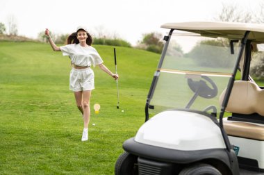 Güzel beyaz kadın golfçü golf arabasının yanında poz veriyor.