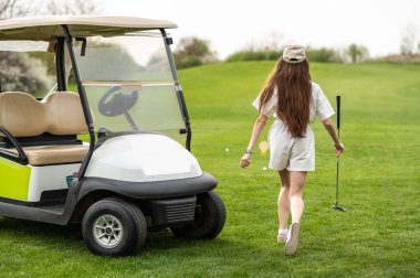 Golf sahasında golf ekipmanıyla arabasının yanında poz veren tanınmayan bir kadın golfçü.