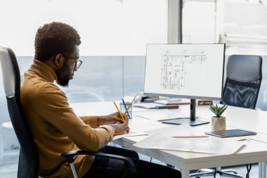 Yetenekli Afrikalı Amerikalı mimar işyerindeki bilgisayarda yeni projeler için planlar yapıyor.