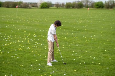Golf oynuyordum. Koyu saçlı genç adam golf kulübünde antrenman yapıyor.