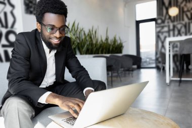 Yoğun bir gün. Koyu tenli, kendinden emin iş adamı laptopta çalışıyor ve meşgul görünüyor.