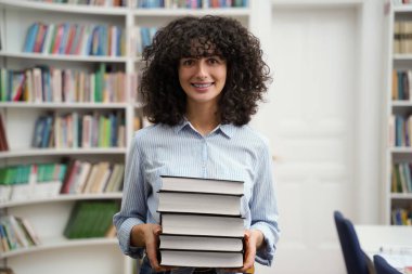Kitapları olan kadın. Elinde kitap yığınıyla gülümseyen kadın kütüphaneci.