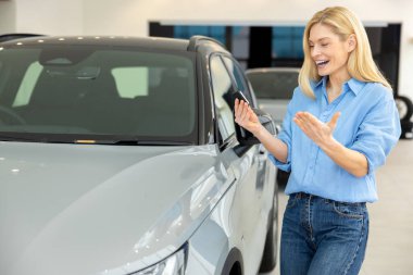 Mutlu hissediyorum. Güzel, uzun saçlı, sarışın bir kadın yeni bir arabanın yanında keyifli ve heyecanlı görünüyor.