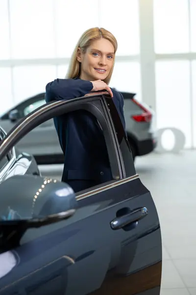 stock image In a car showroom. Elegant beautiful woman near the new car in a showroom