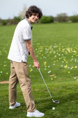 Golfçü. Golf sopasıyla dosyalanmış genç bir adam.