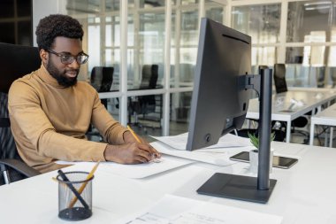 Çalışıyorum. Ofisteki dizüstü bilgisayarda çalışan koyu tenli genç adam.