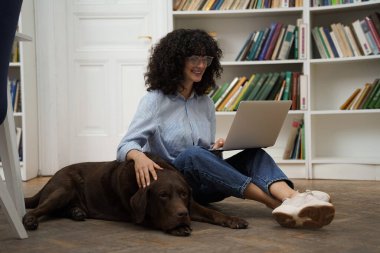 Arkadaşınla çalış. Dizüstü bilgisayarı olan kıvırcık saçlı bir kadın yerde oturuyor, yanında da bir köpek.