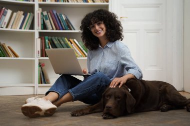 Arkadaşınla çalış. Dizüstü bilgisayarı olan kıvırcık saçlı bir kadın yerde oturuyor, yanında da bir köpek.