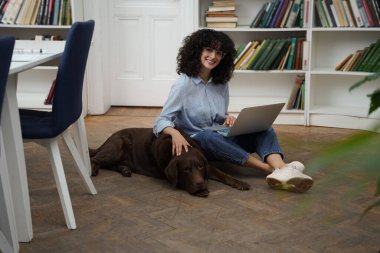 Arkadaşınla çalış. Dizüstü bilgisayarı olan kıvırcık saçlı bir kadın yerde oturuyor, yanında da bir köpek.