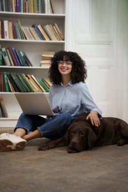 Bir arkadaşla. Dizüstü bilgisayarda çalışan ve yanında yatan köpeğini okşayan hoş bir kadın.