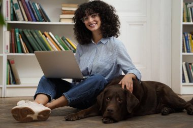 Bir arkadaşla. Dizüstü bilgisayarda çalışan ve yanında yatan köpeğini okşayan hoş bir kadın.