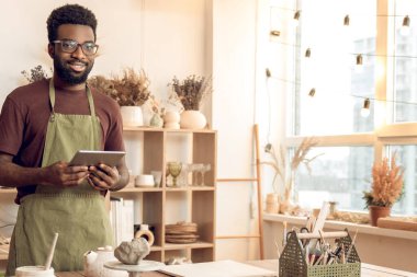 Heykeltıraş. Elleri ıslak, koyu tenli heykeltraş memnun görünüyor.