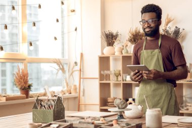 Heykeltıraş. Elleri ıslak, koyu tenli heykeltraş memnun görünüyor.