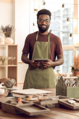 Heykeltıraş. Elleri ıslak, koyu tenli heykeltraş memnun görünüyor.