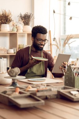 Giyin. Koyu tenli heykeltraş yeni bir ürünü bir ağ üzerinde gösteriyor.