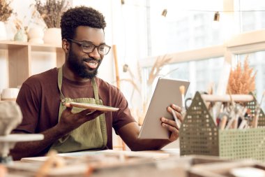 Giyin. Koyu tenli heykeltraş yeni bir ürünü bir ağ üzerinde gösteriyor.