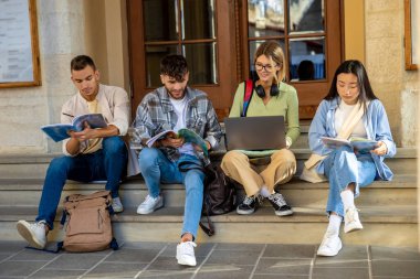 Çok ırklı bir grup öğrenci merdivenlerde birlikte otururken seminere hazırlanıyor.