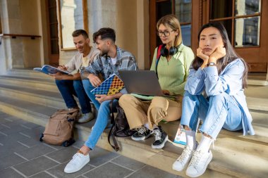 Dizüstü bilgisayarlı genç üniversite öğrencileri üniversite kampüsünün merdivenlerinde oturuyor.