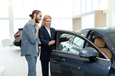 Bir galeride müşteri. Müşteriye yeni bir araba gösteren bir bayide kadın satış asistanı.