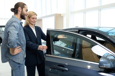 Bir galeride müşteri. Müşteriye yeni bir araba gösteren bir bayide kadın satış asistanı.