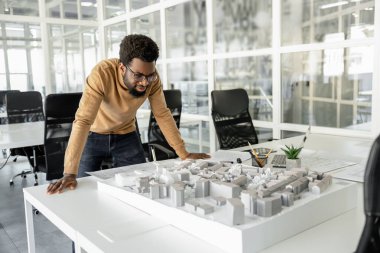 Modelleme. Koyu tenli kıvırcık saçlı mimar model üzerinde çalışıyor ve odaklanmış görünüyor.