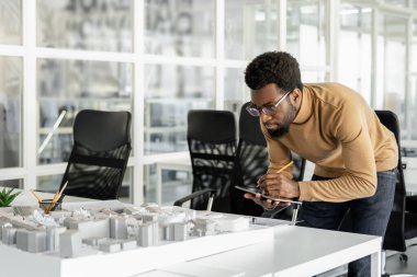 Modelleme. Koyu tenli kıvırcık saçlı mimar model üzerinde çalışıyor ve odaklanmış görünüyor.