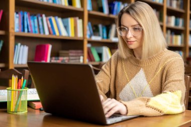 Kütüphanede. Kütüphanede dizüstü bilgisayarda çalışan genç sarışın kadın.