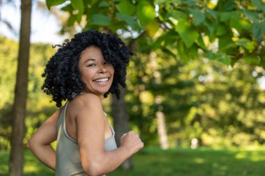 Temiz havada egzersiz yapmak. Parktaki güzel kıvırcık saçlı kadın antrenman yapıyor ve mutlu görünüyor.