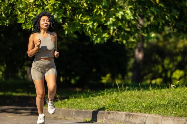 Sabah koşusu. Yazın spor giyimli bir kadın güneşli bir pistte koşuyor ve odaklanmış görünüyor.