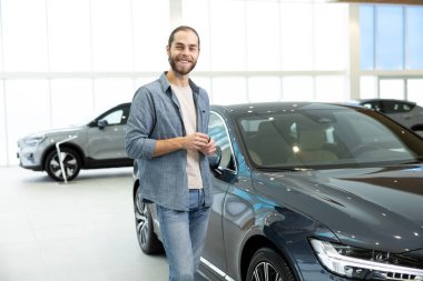 Yeni araba. Arabanın yanında rahat giysiler içinde kendinden emin genç bir adam var.