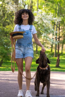 Bir köpekle yürüyüşe çık. Parkta köpeğiyle yürüyüşe çıkmış şortlu sıska genç bir kadın.