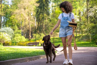 Bir köpekle yürüyüşe çık. Parkta köpeğiyle yürüyüşe çıkmış şortlu sıska genç bir kadın.