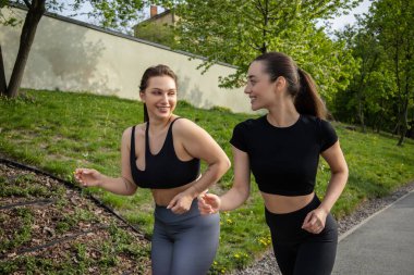 Parkta spor kıyafetleri içinde koşan, açık hava sporlarından hoşlanan Kafkasyalı mutlu bayan arkadaşlar.